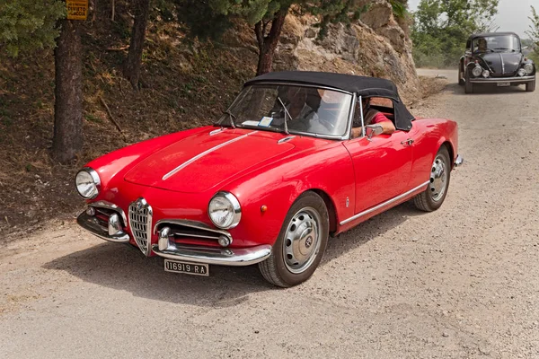 vintage car Alfa Romeo Giulietta Spider runs on a dirt road in the italian hills during the rally 