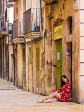 İspanya Tatil serisi. Tarragona dar sokakta. Sarı tuğla duvar ve seyahat, yaz, tatil, gençlik, güzellik konusu döşeli kaldırıma yakın beyaz bezelye kırmızı elbiseli Genç kız.