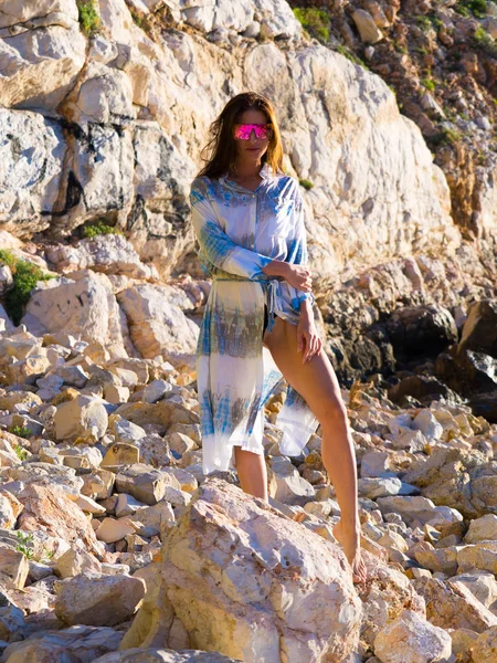 Spain vacation series. Young girl in white and blue dress in sunglasses a rocky beach on subject of travel, summer, vacation, youth, beauty.