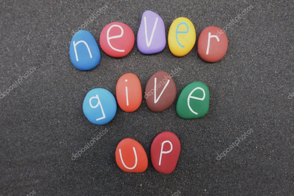 Never give up, motivational message with colored stones text over black volcanic sand