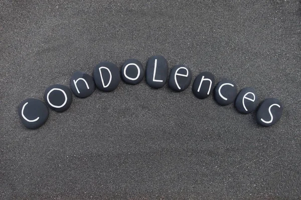 Condolences text with black painted stones over black volcanic sand