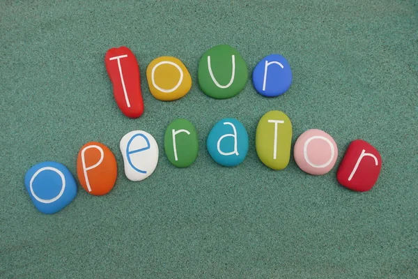 Tour Operator text composed with multi colored stones over green sand
