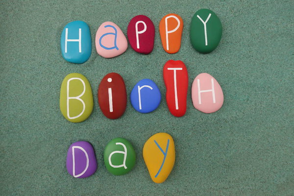 Текст поздравления с днем рождения с разноцветными камнями на зеленом песке
