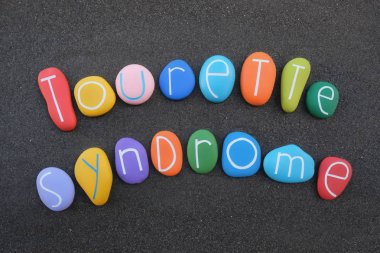 Tourette Sendromu, nörogelişimsel bozukluk, siyah kum üzerinde çok renkli taşlarla oluşturulmuş metinler.