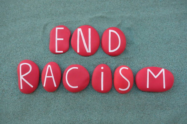 "Покончим с расизмом", текст социальной тематики с красными каменными буквами поверх зеленого песка
