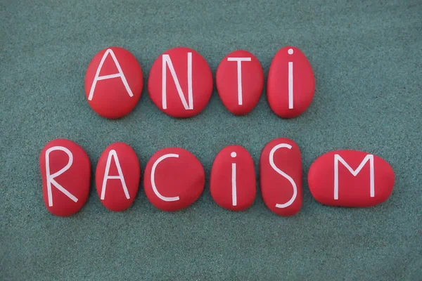 Anti Racism, social issue slogan text composed with red colored stone letters over green sand