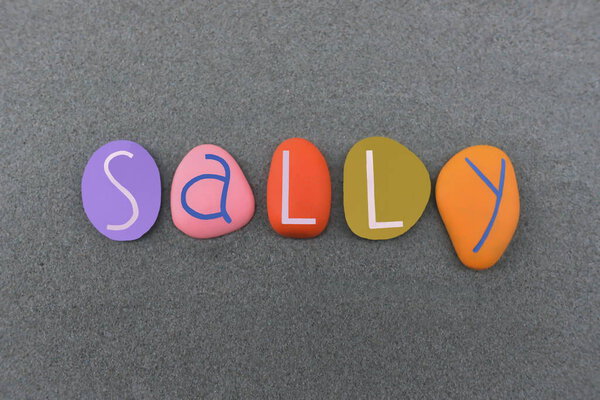 Салли, женское имя составлено из разноцветных каменных букв на зеленом песке
