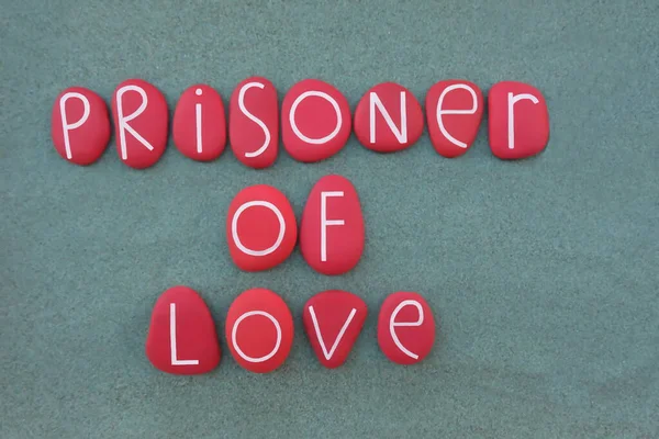 Prisoner of love, negative thoughts composed with red colored stone letters over green sand