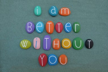 Sensiz daha iyiyim. Yeşil kumların üzerinde çok renkli taş harflerle yazılmış negatif slogan.