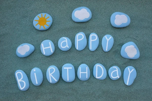 Happy Birthday text composed with blue colored stone letters over green sand