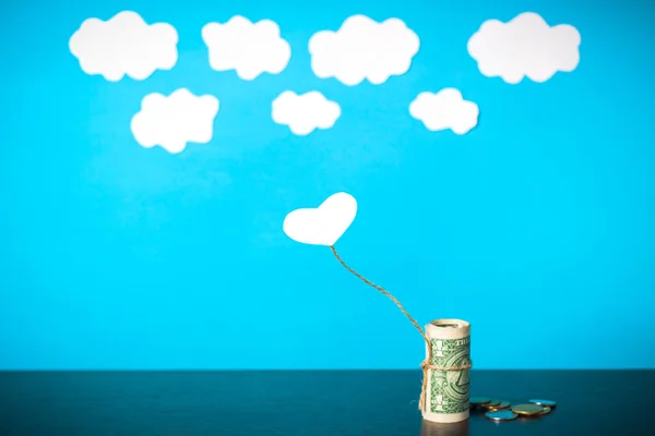a heart connected with money trying to fly away into the clouds