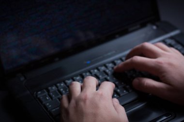 Internet hacker hırsız kavramı. Hacker dizüstü bilgisayar ekipmanı saldırmak için kullanma. Karanlık ve korkunç aydınlatma. Bir sürü bilgisayar ekranında sembolleri. Seçici odak.