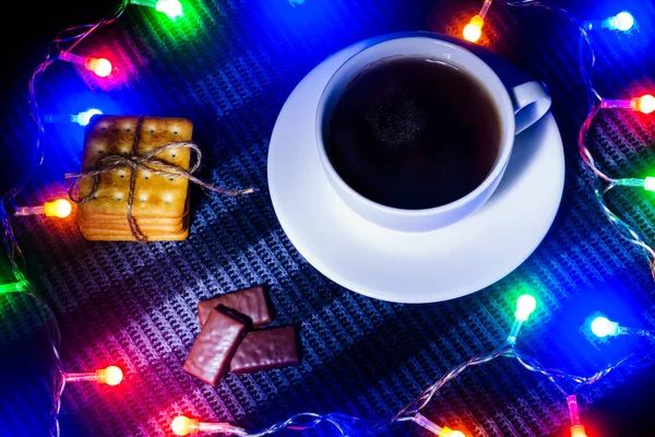 concept new year. Christmas story. a cup of hot tea and cookies and candy in a frame of Christmas garland. dark lighting. view from above. fog for fairytale atmosphere and miracles