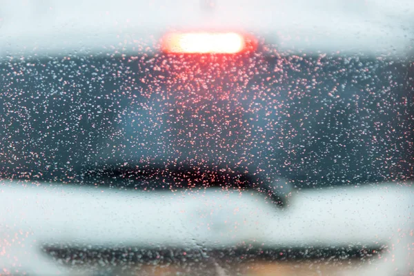 drops on the windshield of the car in the box. a blurred white car at background. Layout for decor and design at transportation. weather conditions and traffic safety on the road.  out of focus.