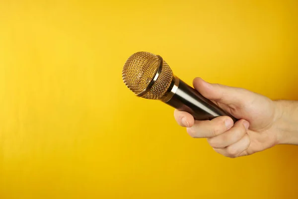 Złoty Mikrofon Pod Ręką Żółtym Tle Pojęcie Żółtych Plotek Przestrzeń — Zdjęcie stockowe