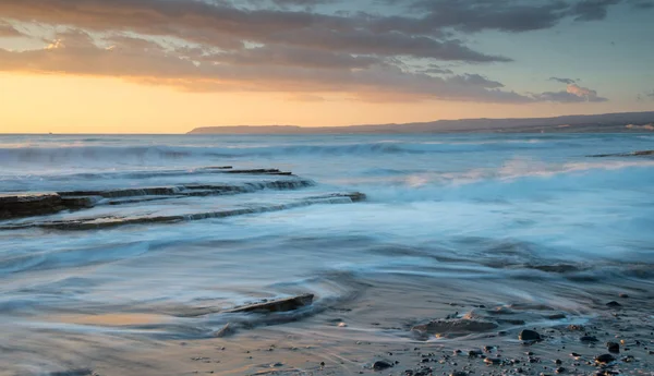 Bir kayalık sahil üzerinde dramatik güzel gün batımı. Uzun pozlama fotoğraf