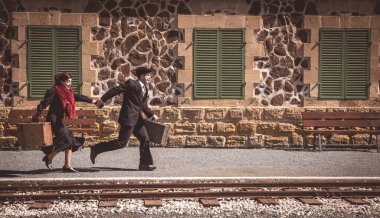 Klasik valizli genç çift tren istasyonunun dışında hızla koşuyor ve son trene yetişiyor..