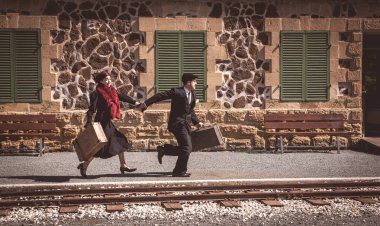 Klasik valizli genç çift tren istasyonunun dışında hızla koşuyor ve son trene yetişiyor..