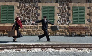 Klasik valizli genç çift tren istasyonunun dışında hızla koşuyor ve son trene yetişiyor..