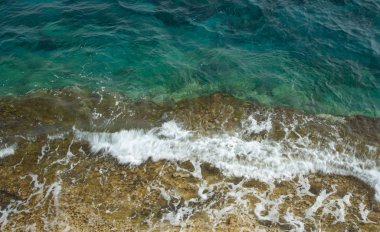 Kayalık bir sahil üzerinde açık mavi sakin deniz suyu arka plan