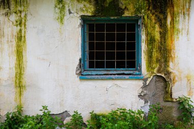 Hasarlı beyaz duvarda metal çerçeveli kırık mavi pencere