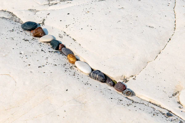 Kleine Strandkieselsteine in einer Reihe auf einer felsigen weißen Oberfläche. — Stockfoto