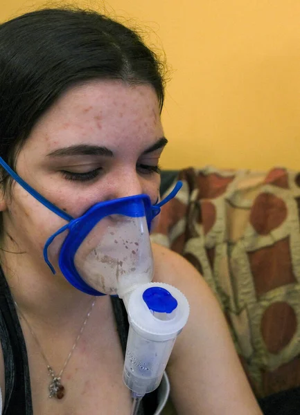 Young woman inhaling through inhaler mask for asthma therapy on the coach at home