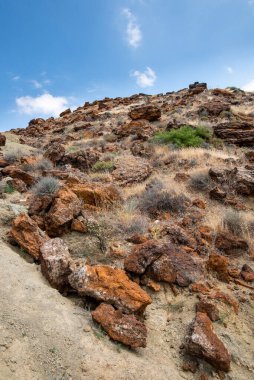 Uçurumunda büyük kayalar ve mavi bulutlu gökyüzü olan terk edilmiş bir bakır madeninin kuru arazisi.
