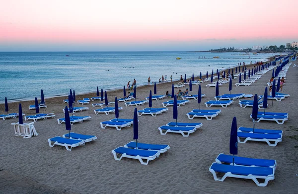 Plage vide avec sable doré, parasols fermés et au coucher du soleil. — Photo