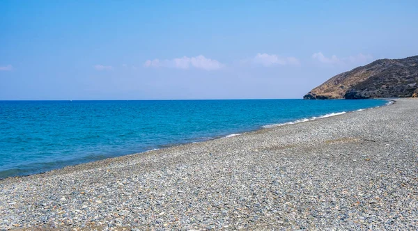 Praia de seixos vazia com água calma azul contra o céu azul — Fotografia de Stock