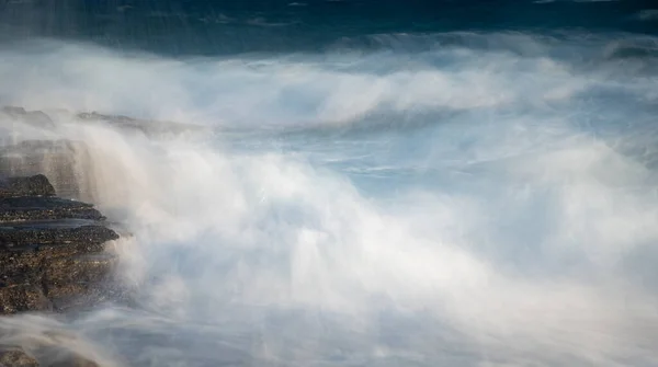 Spritzende stürmische, windige Meereswellen an einer felsigen Küste — Stockfoto