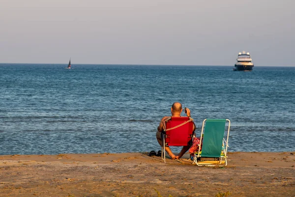 Невідомий чоловік сидить на піщаному пляжі, насолоджуючись морем на заході сонця . — стокове фото