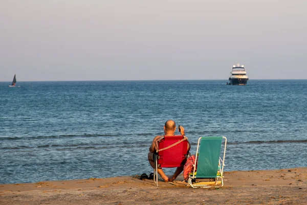 Uomo non riconosciuto seduto su una spiaggia sabbiosa che si gode il mare al tramonto. — Foto Stock