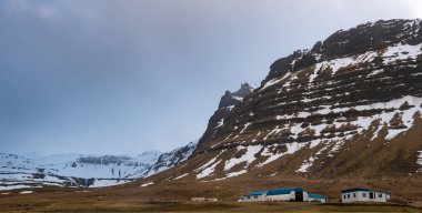 İzlanda 'da karla kaplı dağın eteğinde uzak bir çiftlik evi var. İzlanda manzarası