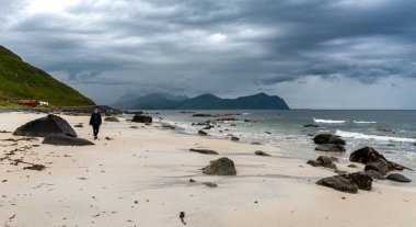 Norveç 'in Lofoten adalarındaki Vikten Strand kumsalında dramatik bulutlu bir gökyüzünün altında yürüyen bir kadın.