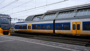 Tren istasyonunda birden fazla tren var. Bir tren hareket halinde, diğeri de park halinde. şehir ulaşımı Amsterdam merkez tren istasyonu.
