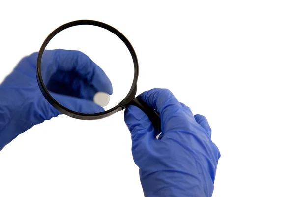 Büyütme altında beyaz bir arka plan üzerinde ilaçtır. Elinde mavi eldiven.