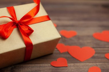 Kırmızı kurdele ve kalpleri ahşap arka plan üzerinde hediye kutusu