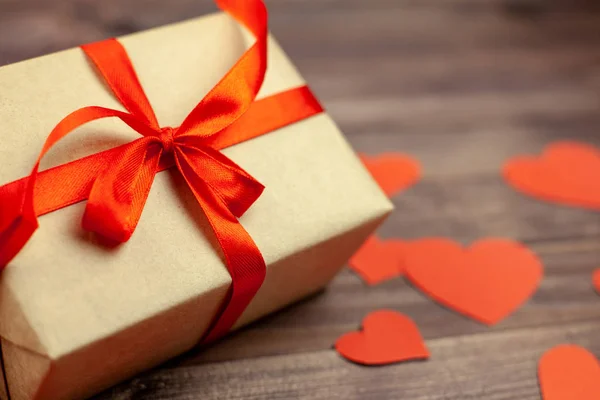 Kırmızı kurdele ve kalpleri ahşap arka plan üzerinde hediye kutusu