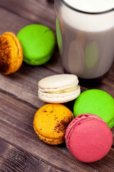Çok renkli macaroons ve bir bardak süt bir ahşap masa üstü üzerinde göster