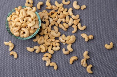 Kavrulmuş kaju fıstığıyla dolu yeşil bir kase. Gri bir yüzeye yerleştirilmiş. Doğal ve iştah açıcı bir görünüş için etrafa saçılmış birkaç fındık..