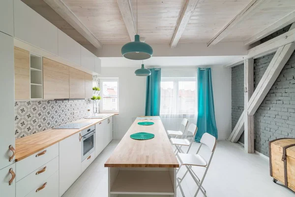 モダンな白いキッチン キャビネット誘導コンロ 白い家具で明るいキッチンに アイランド キッチン ターコイズ ブルーのランプ カーテン モダンで明るいアティック アパートメント — ストック写真