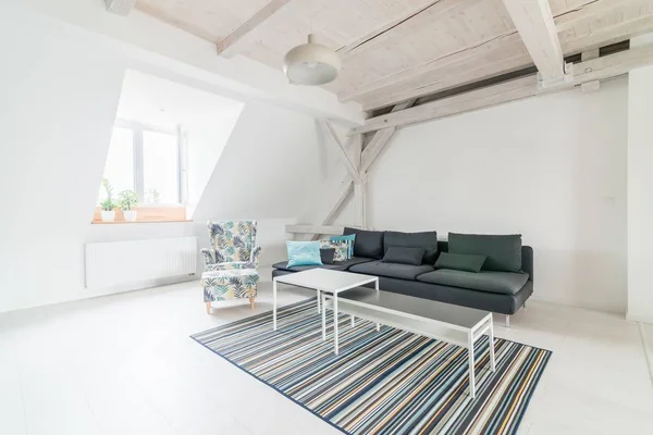 Bright attic living room with wooden ceiling beams. Grey fabric sofa. Modern, bright attic apartment.