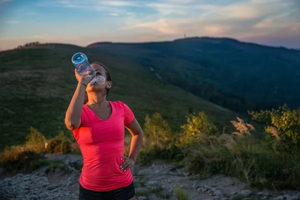 疲倦的妇女足迹赛跑者饮用水从塑料瓶在山里 — 图库照片