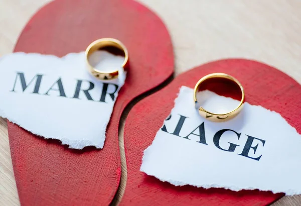 Divorce and separation concept. Two broken golden wedding rings on broken red heart.