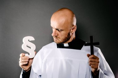 Catholic priest in white surplice holding crucifix and paraphaph. Symbols of law and religion. Church harassment and crime concept clipart