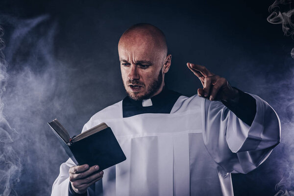 Catholic priest in white surplice and black shirt with cleric collar reading bible and preaching a sermon