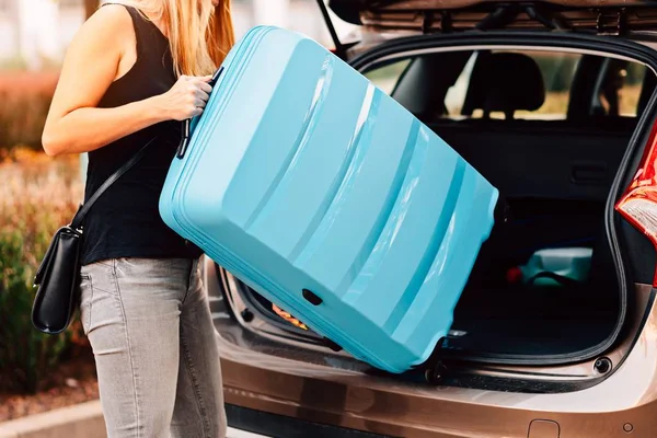 Молодая Женщина Загружает Два Голубых Пластиковых Чемодана Багажник Машины Подготовка — стоковое фото