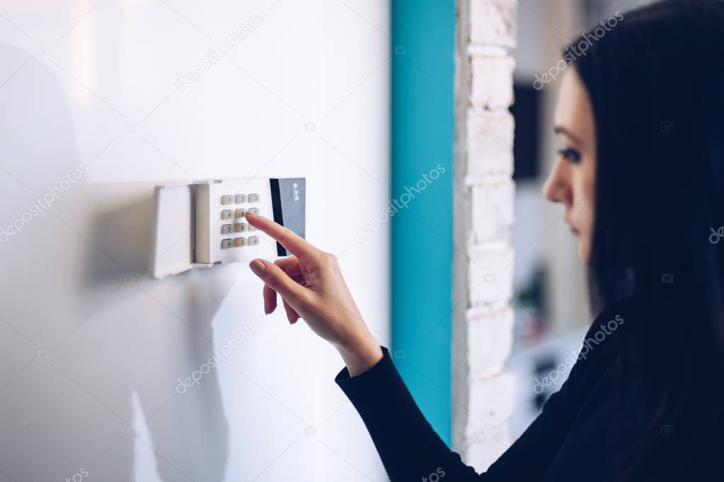 Brunette woman entering security pin on home alarm keypad. Home security system