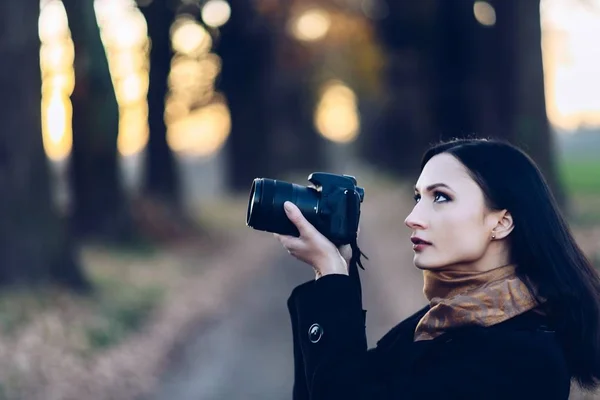 Young brunette woman taking photos with dslr photo camera outdoors